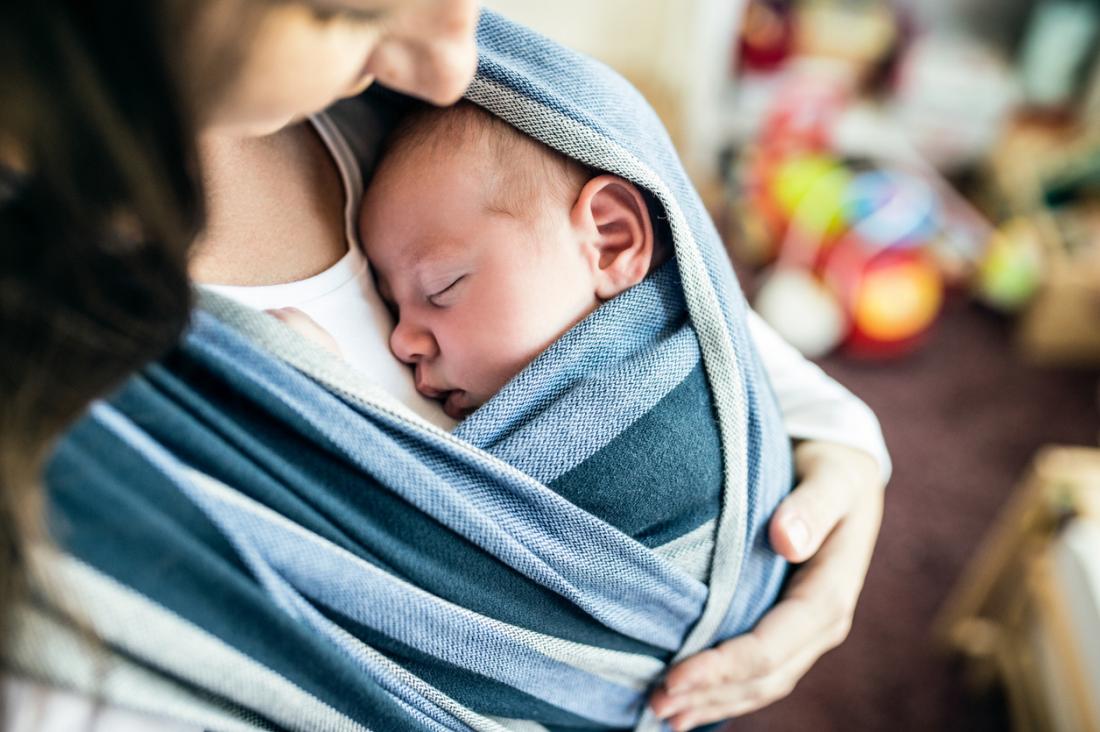 Новороденото бебе се заплита в бебешки носач на гърдите на майката.