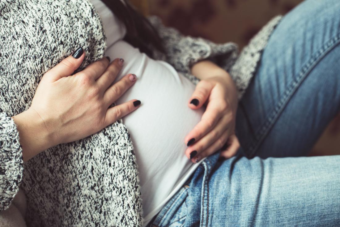 Młoda kobieta we wczesnych stadiach ciąży trzymając się za brzuch.