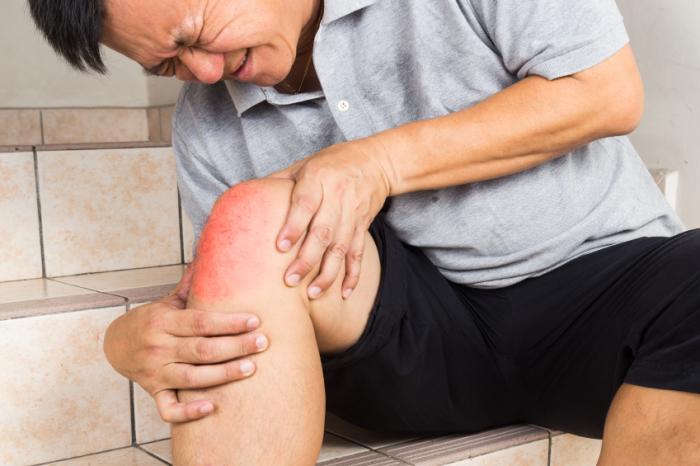 Ein Mann hält ein schmerzhaftes rotes Knie.
