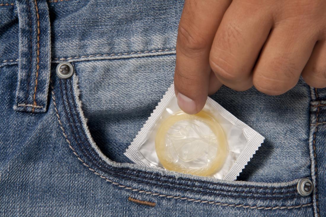 Mężczyzna wyciąga pakiet prezerwatyw spermicide z kieszeni.