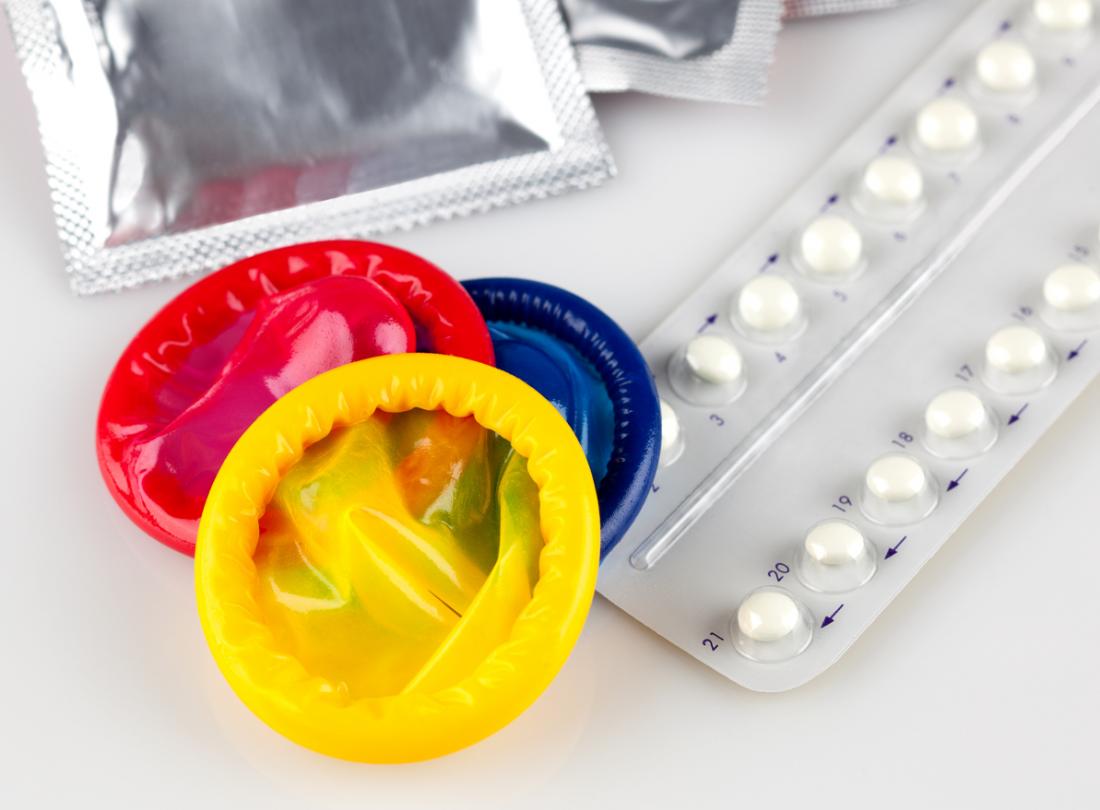 Preservativos espermicidas coloridos ao lado de um pacote de pílulas anticoncepcionais.