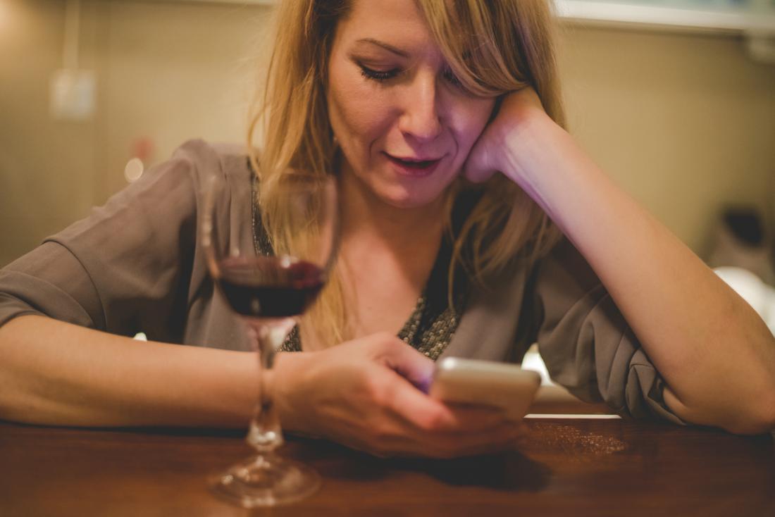 テーブルに赤ワインのガラスと電話を持っている女性