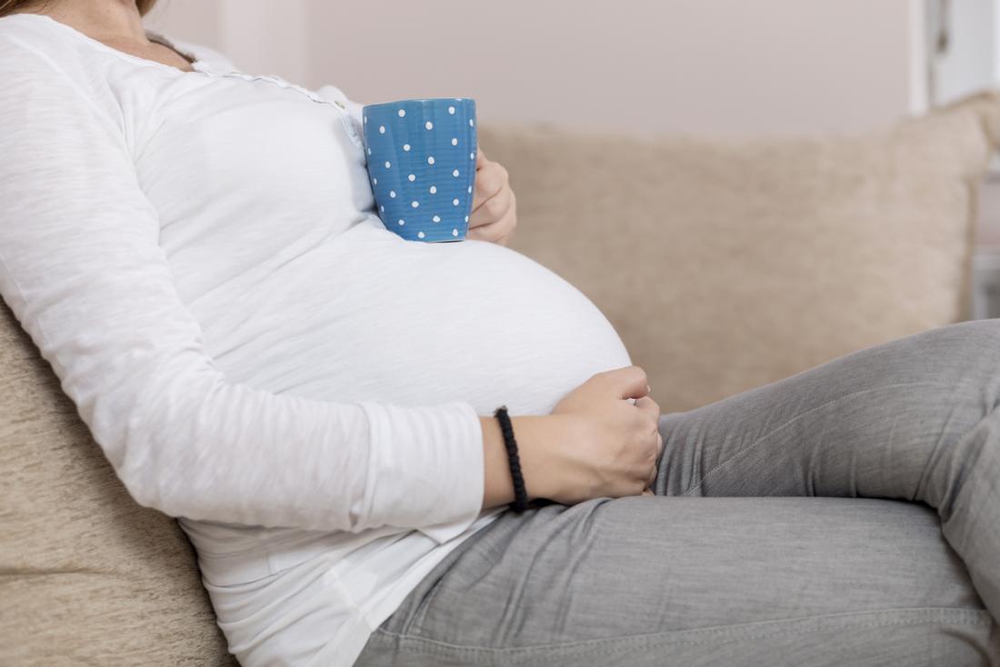 Mulher grávida com uma xícara de chá ou café.