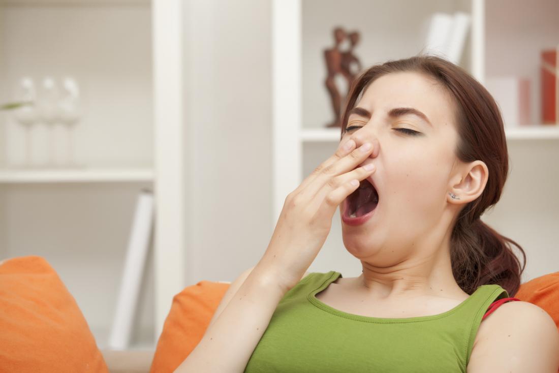 Жена у дома се прозява и покрива устата си.