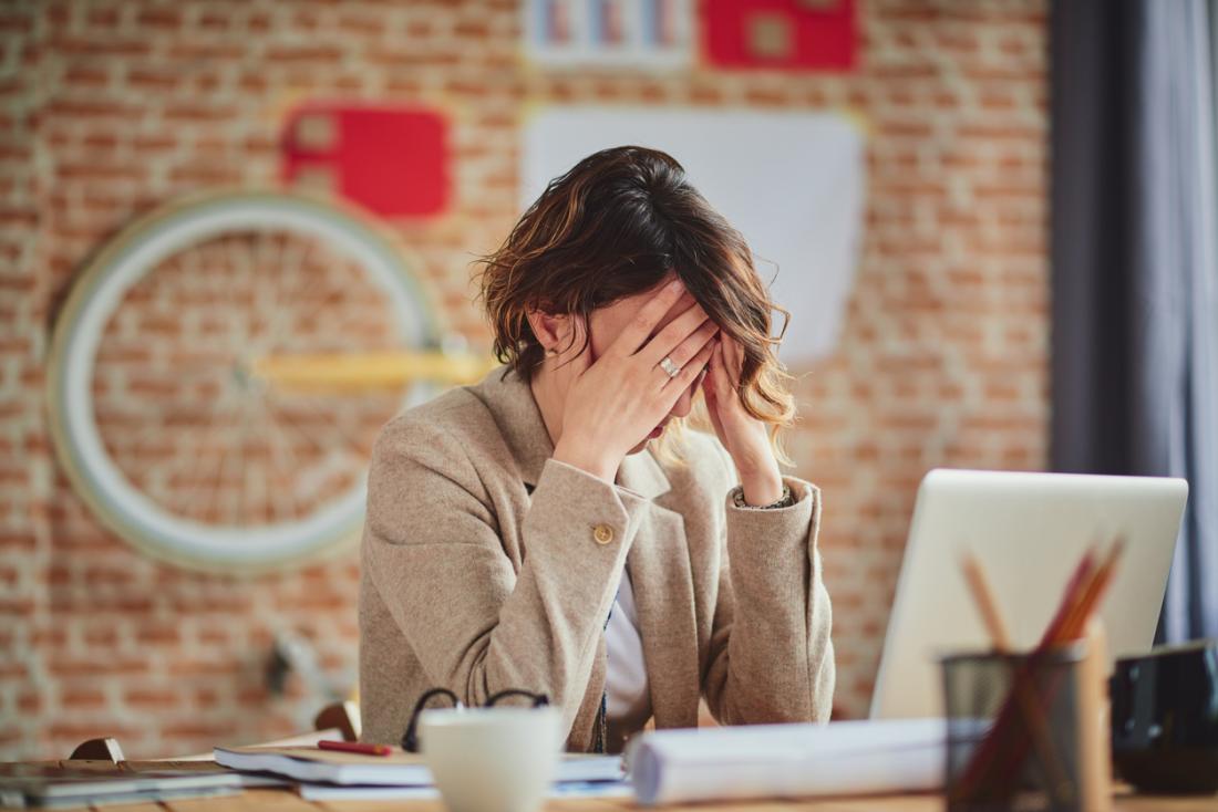 donna stressata e ansiosa al lavoro, stanca e sfregandosi le tempie a causa di un mal di testa.