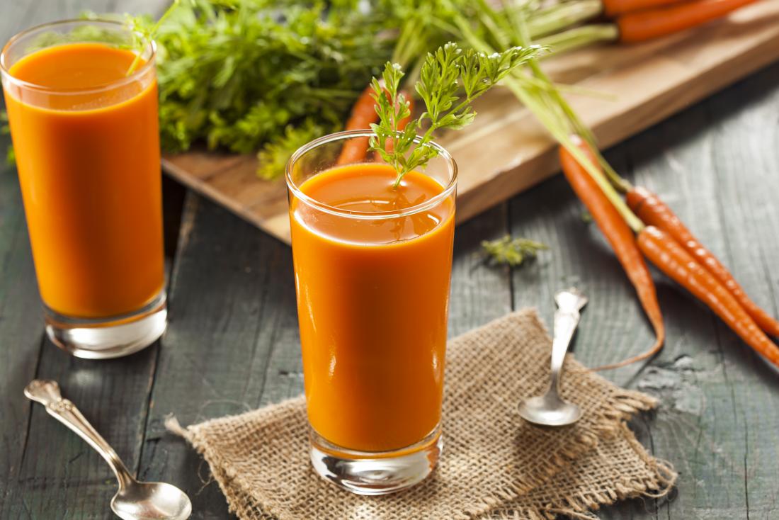 Succo di carota in bicchieri accanto a carote crude sul tagliere.