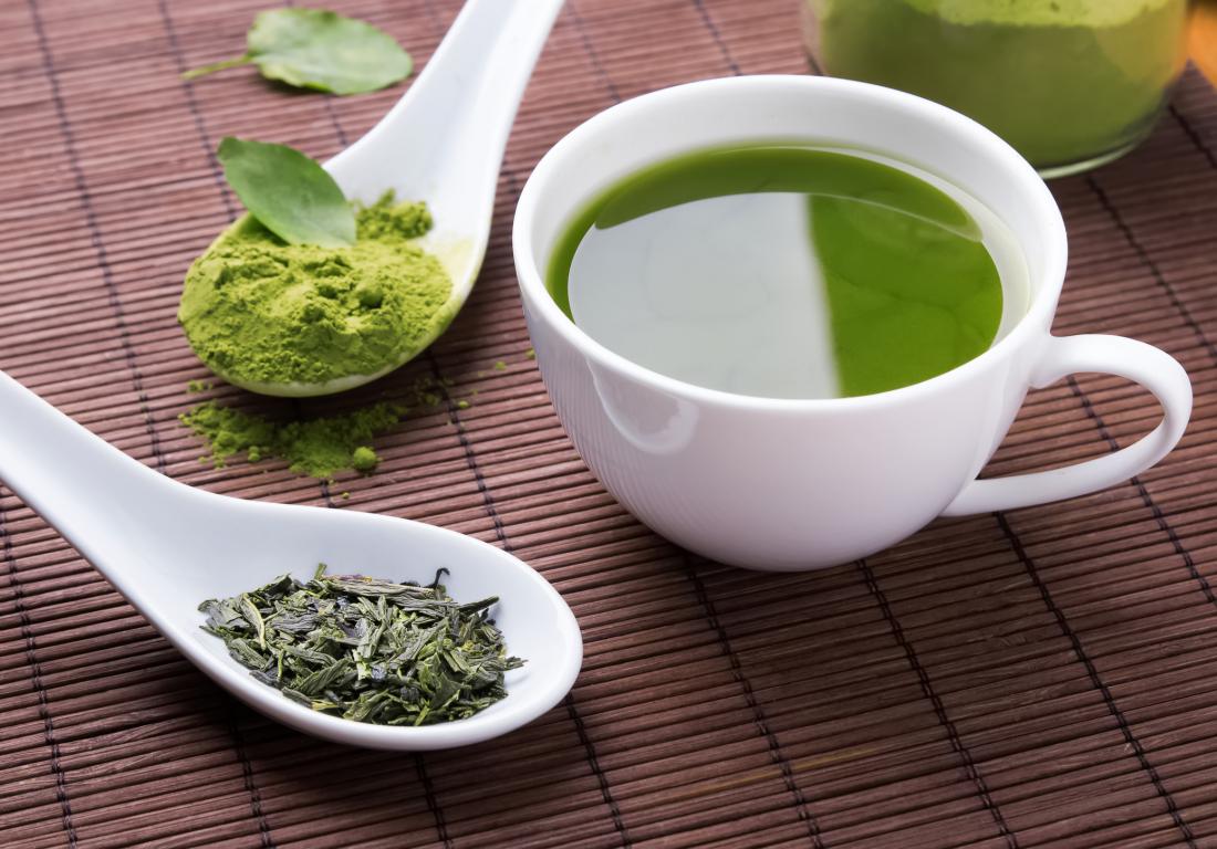 Suppléments à base de plantes sous forme de poudre de matcha et de thé en vrac sur des cuillères, à côté d'une tasse de thé vert.