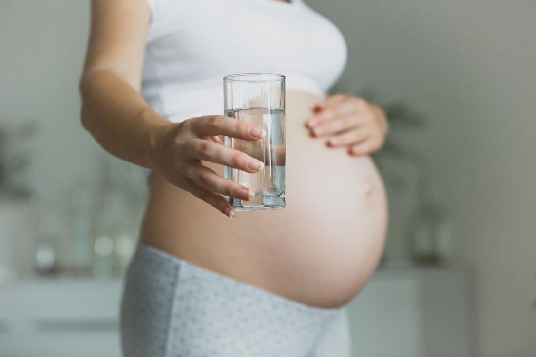 бременна жена, която държи чаша вода