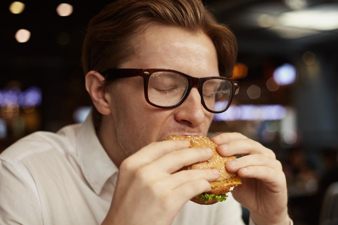 Човек яде хамбургер.
