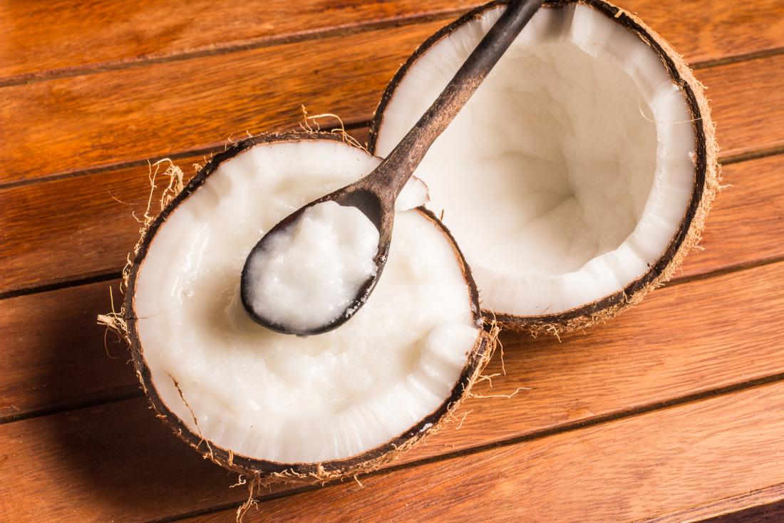 Kokosnussöl auf Holzlöffel, auf halbierte Kokosnuss.