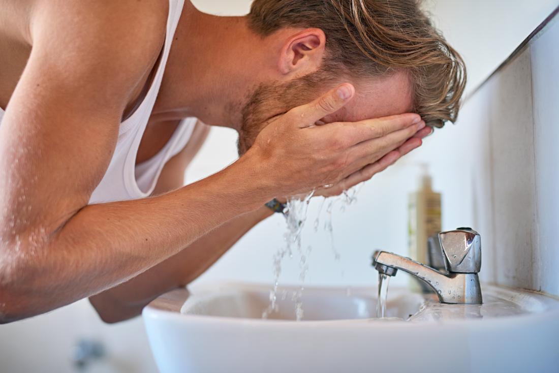 Uomo che si lava la faccia nel lavandino del bagno.