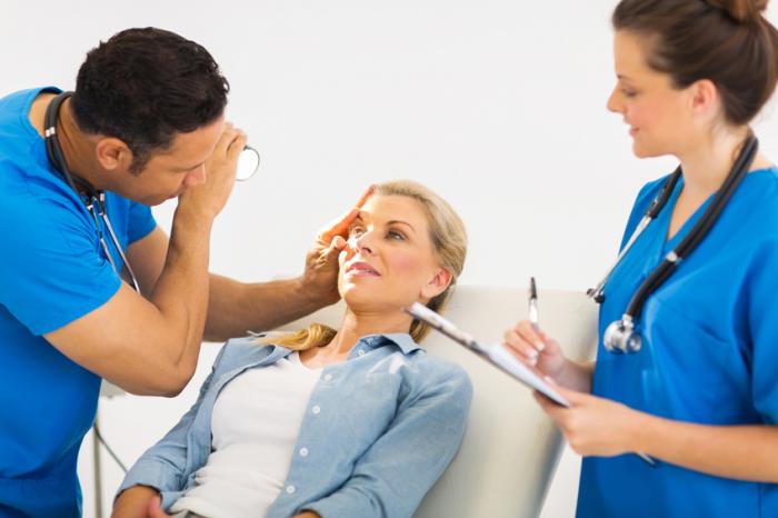 Bir kadın doktor bir kadın hemşire not alırken bir erkek sağ gözü inceler