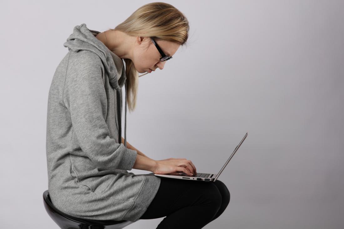 Жена, седнала на стол, използваща лаптоп, с извити рамене и лоша поза.