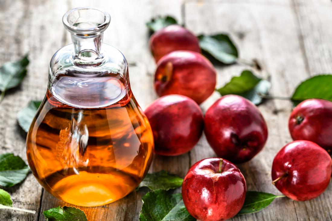 Apfelweinessig in der Glasflasche auf Tabelle mit roten Äpfeln.