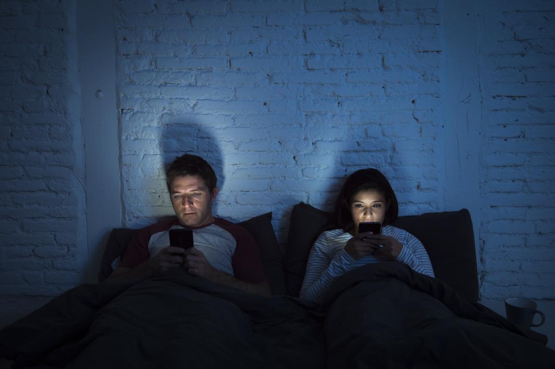 cặp vợ chồng nhìn chằm chằm vào điện thoại của họ trên giường