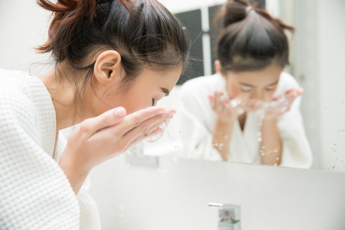 Frau wäscht ihr Gesicht vor dem Spiegel.