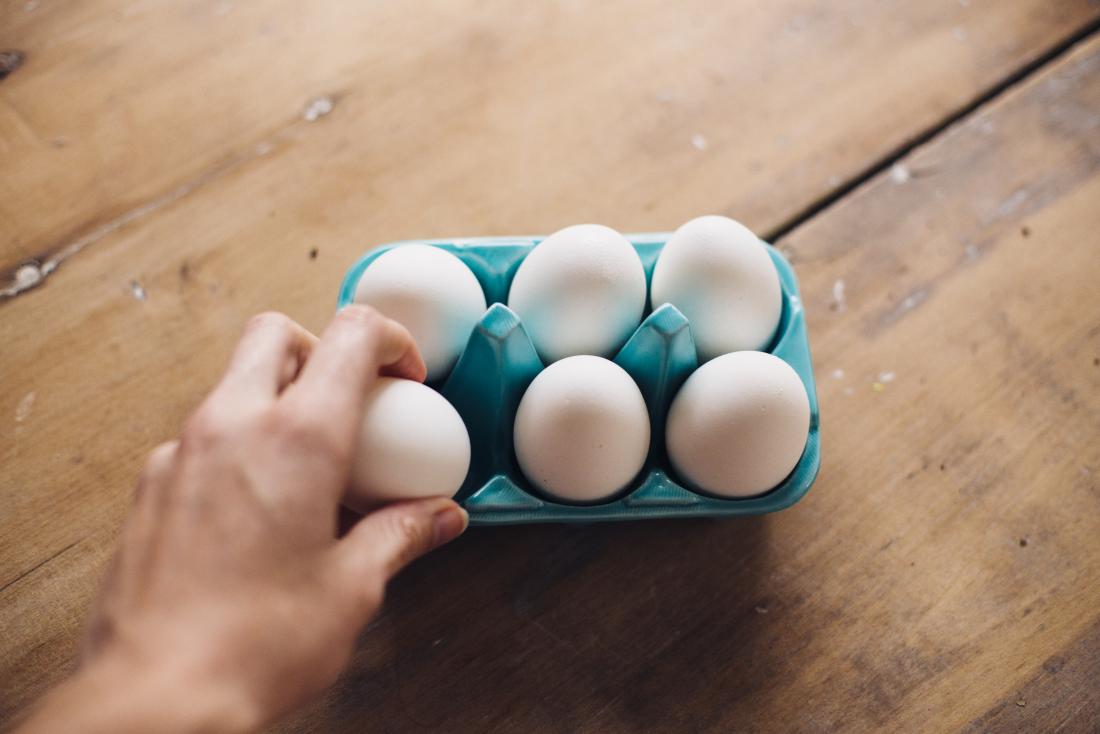 Hand greift nach einem Ei in einer Eierbox