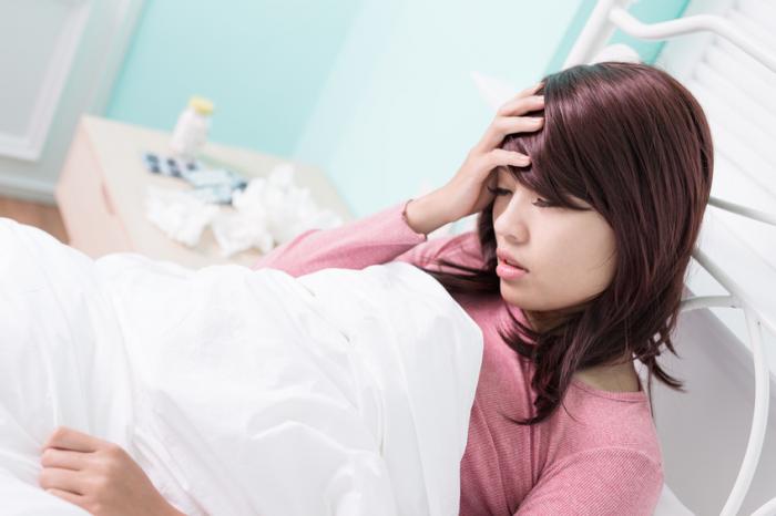 Một người phụ nữ đang nằm trên giường với đau đầu.