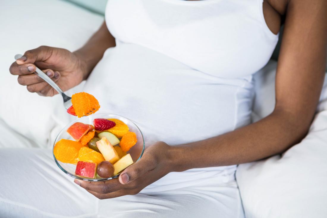 Schwangere Frau, die Schüssel gesunden Fruchtsalat isst.