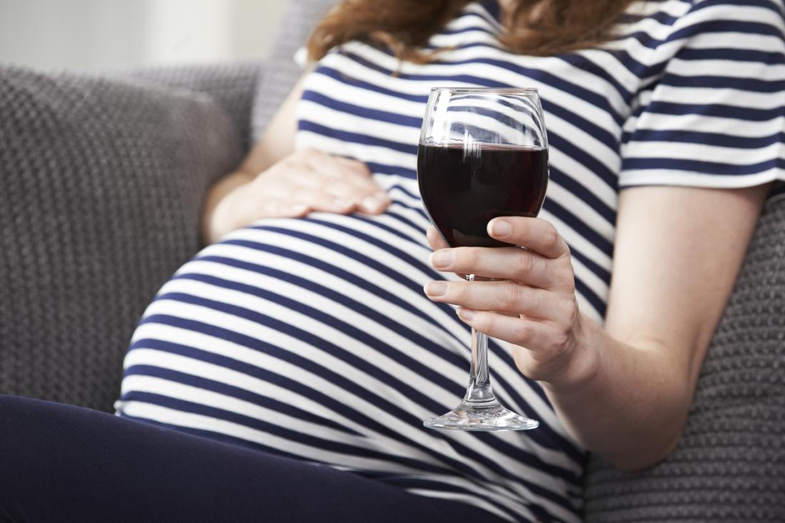 Бременна жена, държаща чаша вино.