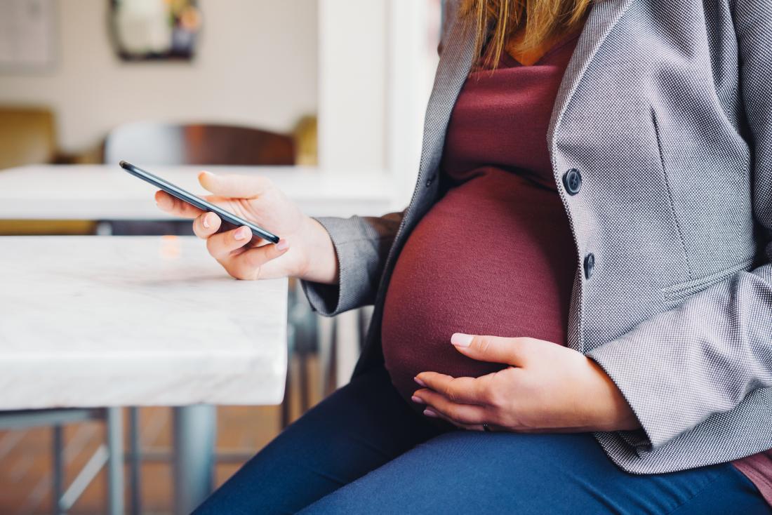 Schwangere Frau, die ihren Schätzchenstoß hält und Telefon betrachtet.