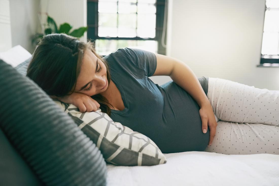 Бременна жена, лежаща на нейната страна, която държи бебешки бум