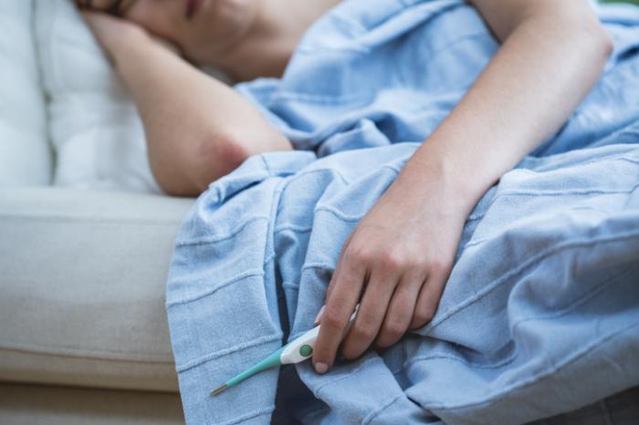 persona a letto con l'influenza in possesso di un termometro