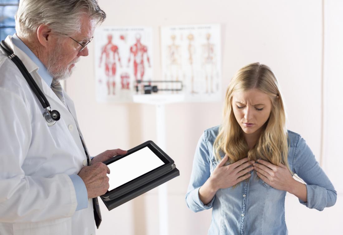 Жена страдаща от гастро-езофагеална рефлуксна болест или ГЕРБ в кабинета на лекаря, която държи гърдите си в болка, докато лекарят прави бележки на таблетка.