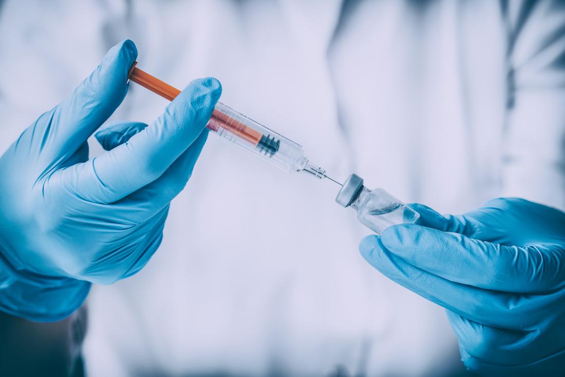 L'ingrédient tiré du vaccin antigrippal est contenu dans une bouteille qui est prise par une seringue dans des mains gantées.