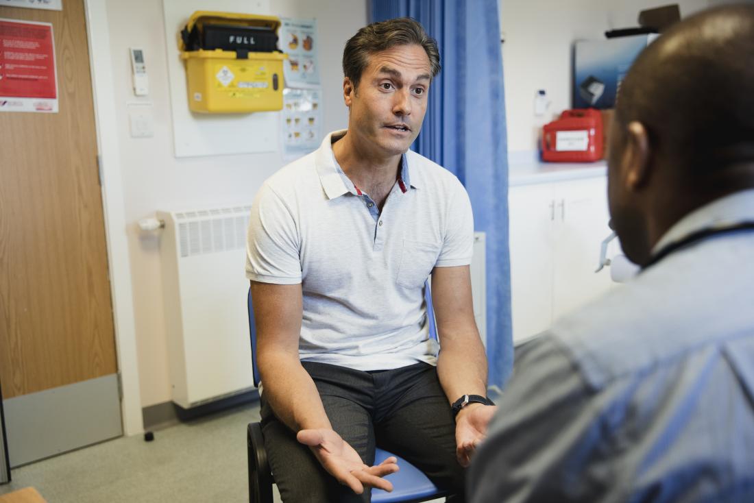 Човек обсъждане на здравен проблем в кабинета на лекар с лекар в преден план.