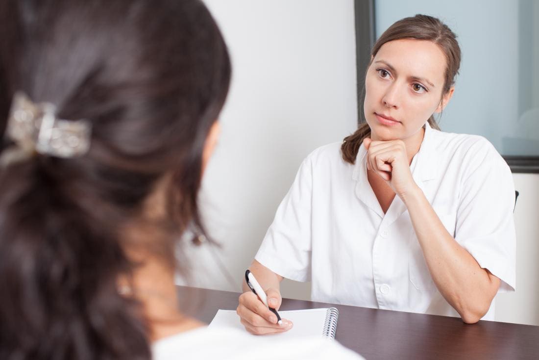 Femme médecin ou gynécologue écoutant avec sympathie une patiente au premier plan.