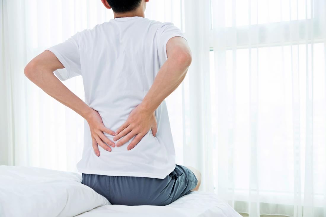 Homme avec douleur à la hanche pendant la nuit assis sur le lit en tenant le bas du dos.