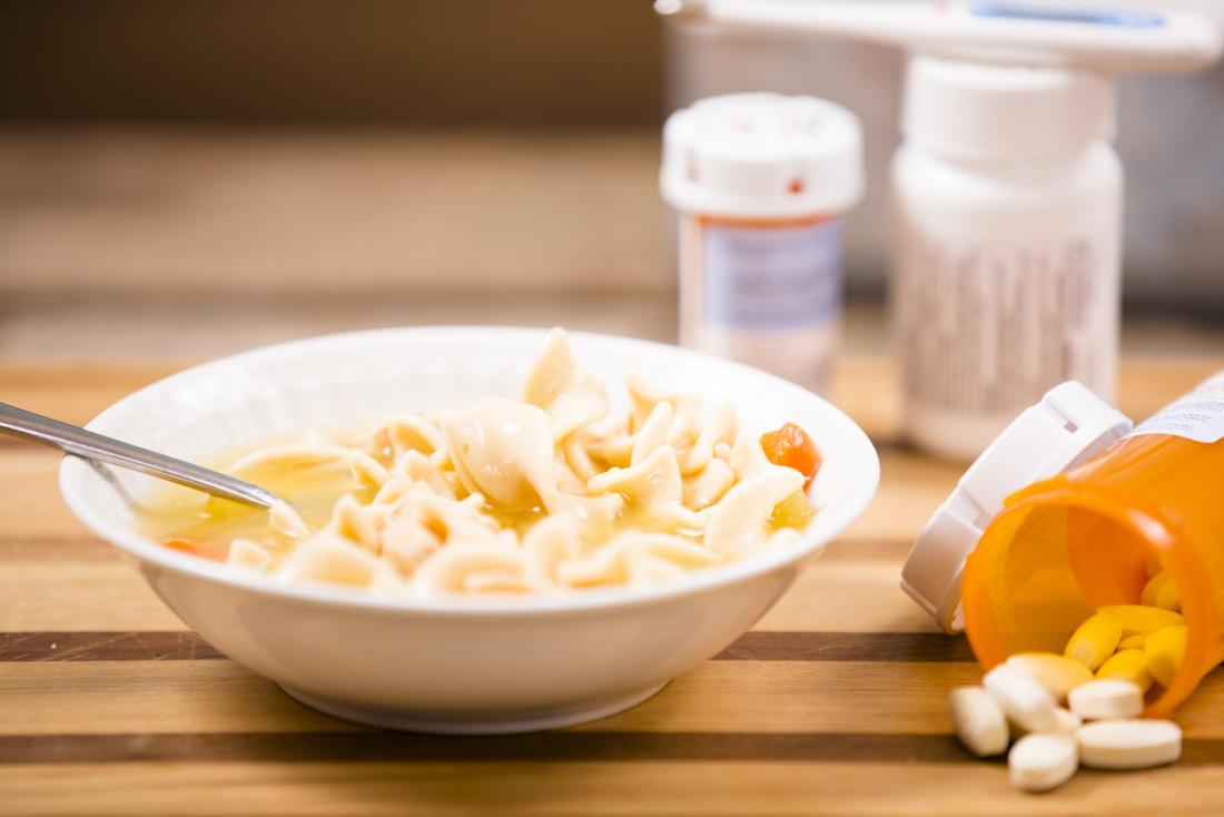 Zuppa calda di pollo in una ciotola accanto a bottiglie di medicinali e pillole.