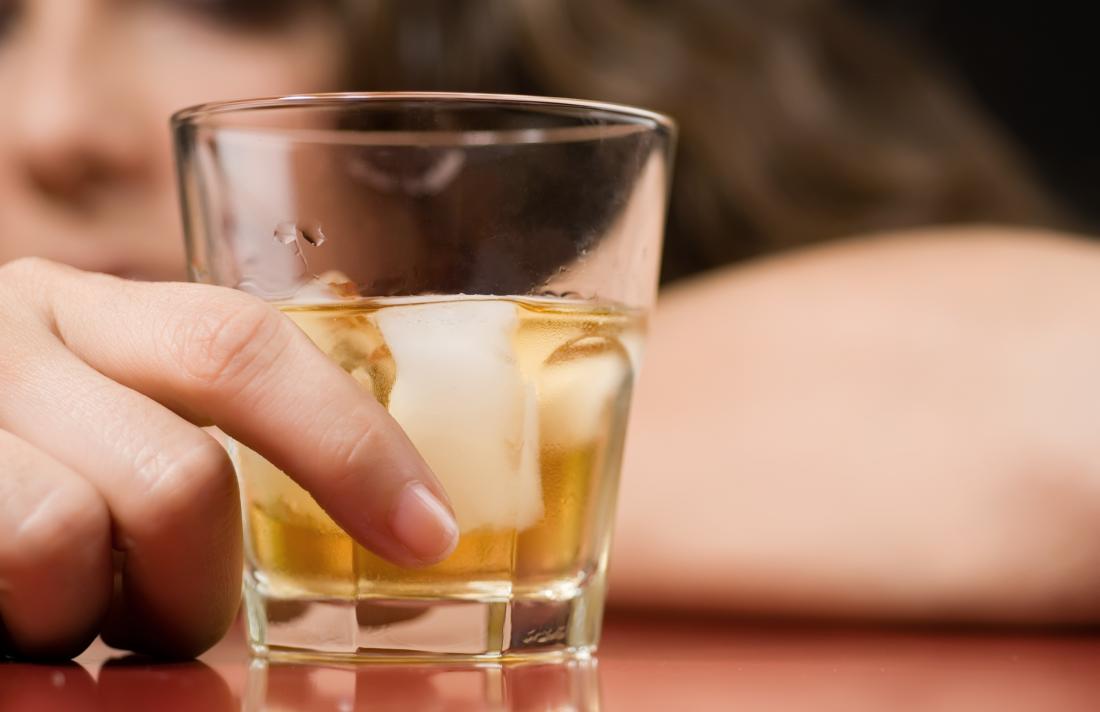 Alkoholische Frau mit einem Glas Whisky vor ihr.