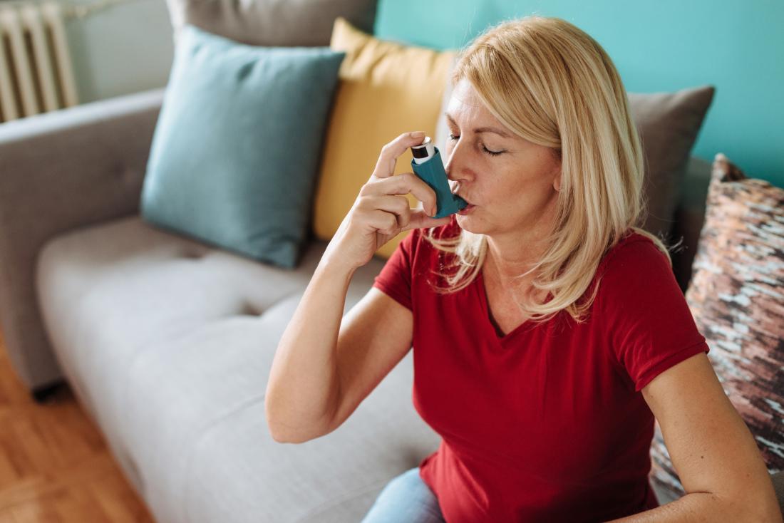 Femme utilisant un inhalateur de secours pour traiter une crise d'asthme à la maison.