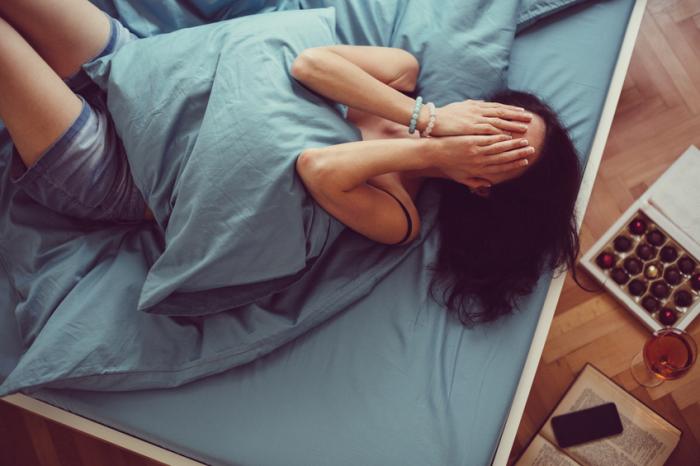 Une femme allongée sur son lit couvrant son visage de ses mains