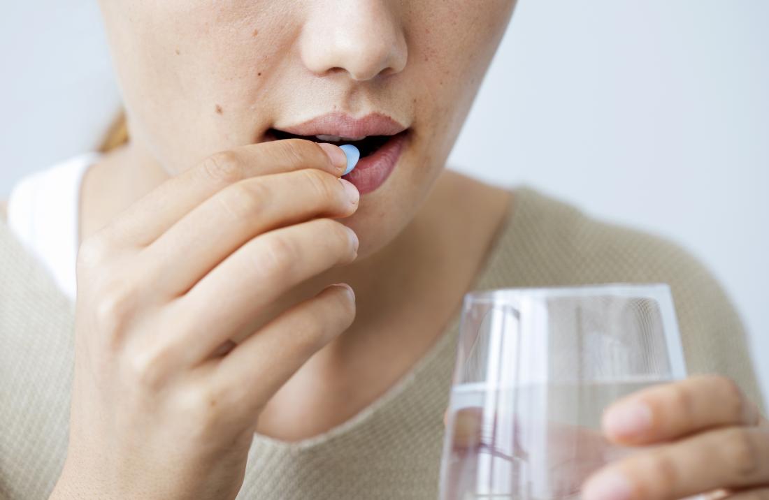 Mulher tomando antibiótico por via oral, mantendo o copo de água.
