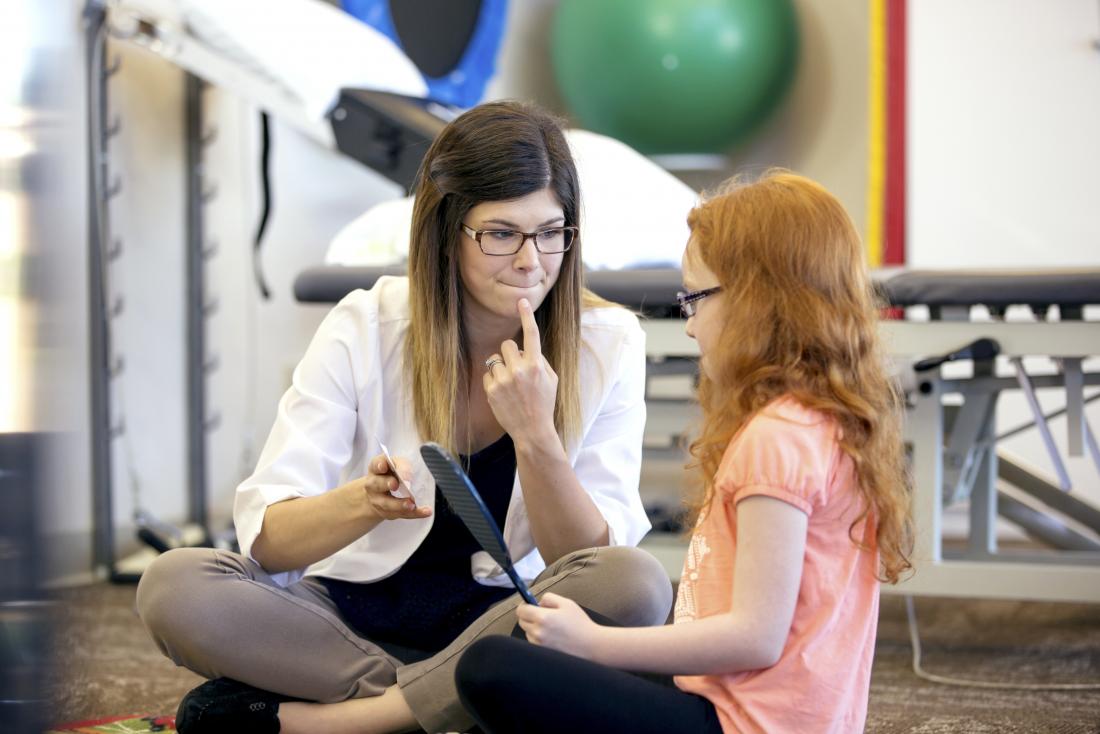 L'orthophonie est menée par un médecin assis avec une jeune fille qui tient un miroir.