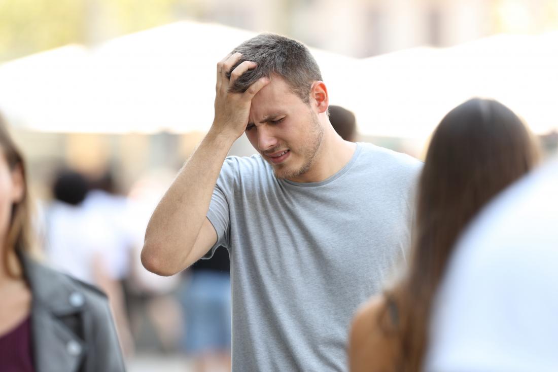 Чувствен и стресиран човек с главоболие или мигрена на обществено място, който държи челото си в болка.