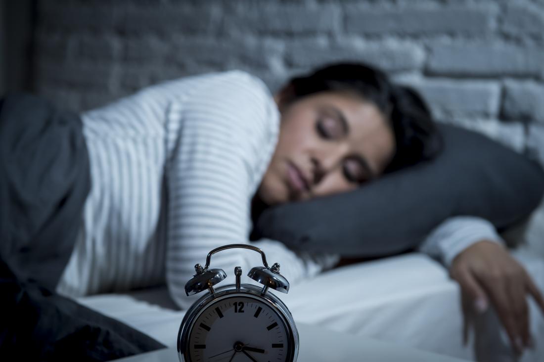 Спящата жена в леглото с алармен часовник на преден план.