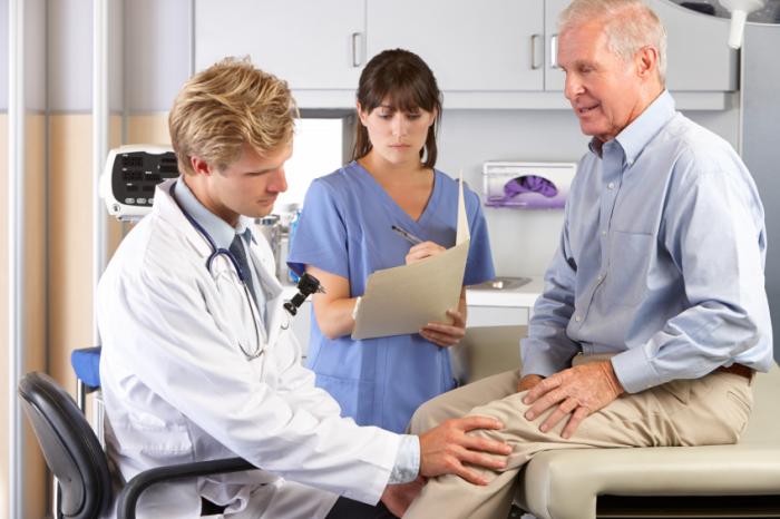Ein Arzt untersucht das Knie eines älteren Mannes.