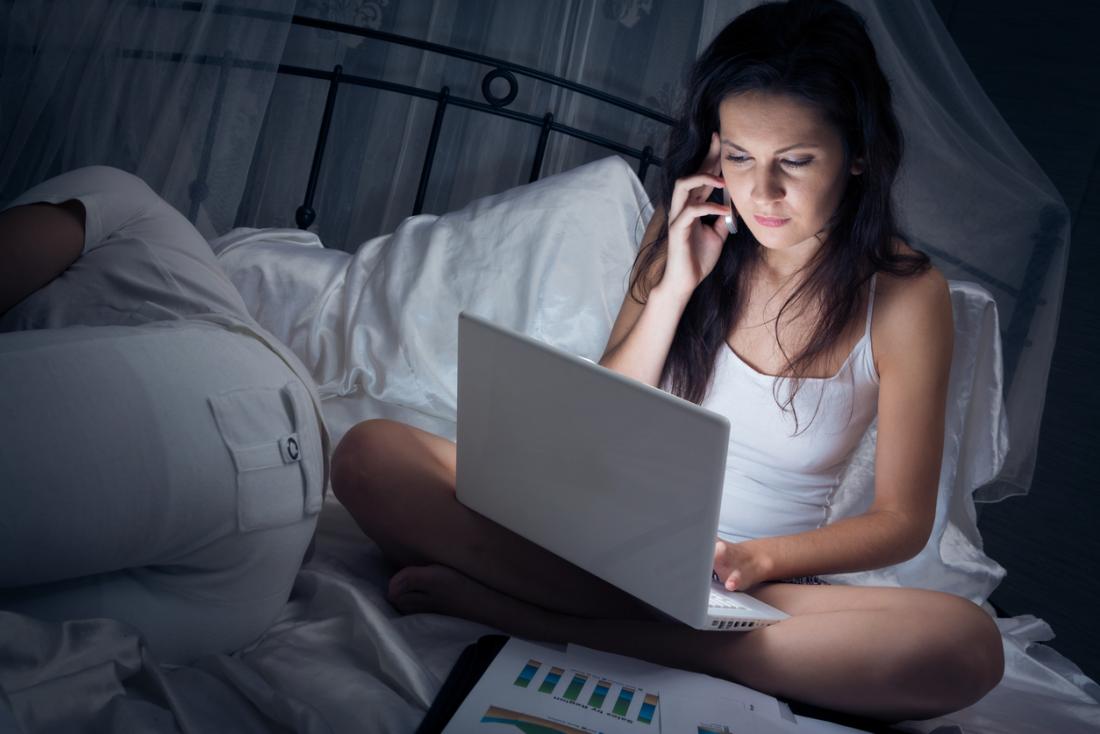 момиче, седнало на легло, използващо телефон и лаптоп