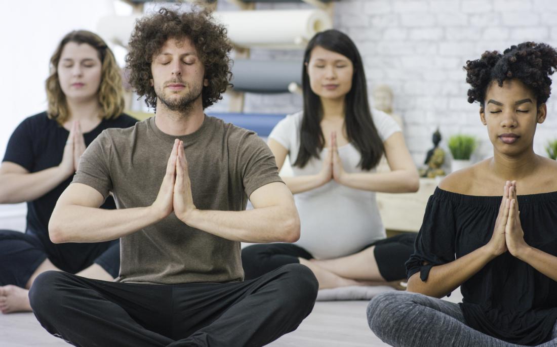 Groupe de cours de yoga posant et méditant.