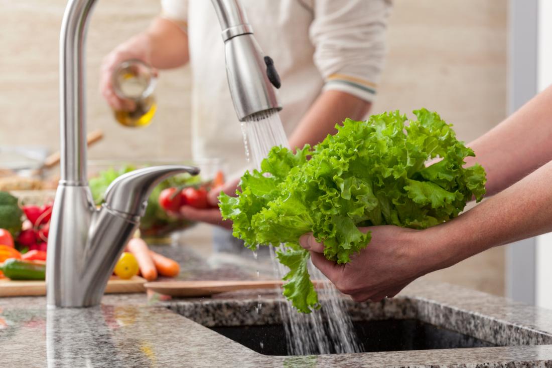 Лице, подготвящо зеленчуци, измивайки къдрави листа от кале под течаща вода в кухнята.