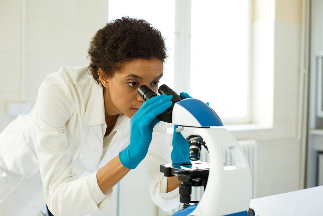 Жена, използваща микроскоп в лабораторията, за да анализира биопсичната проба.