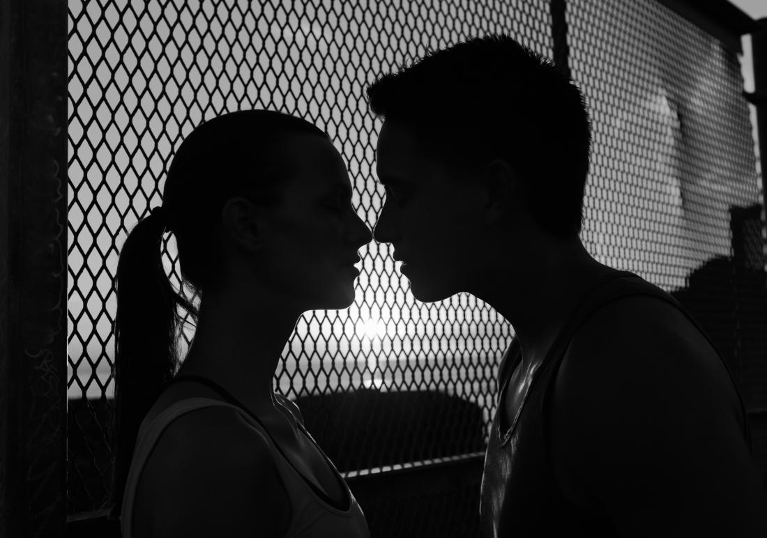 Una silhouette di una coppia che si bacia davanti a un recinto.