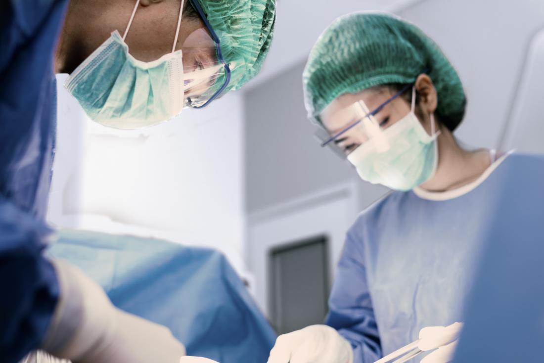Dois cirurgiões no trabalho em sala de cirurgia, realizando cirurgia facial.