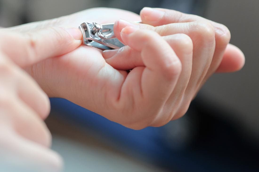 Personne avec des lignes noires sur les ongles coupant les ongles.