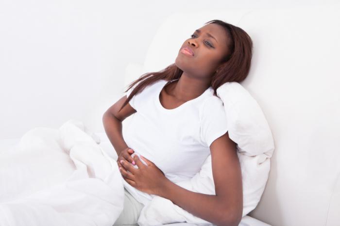 Một người phụ nữ đang nằm trên giường với một cái bụng đau đớn.