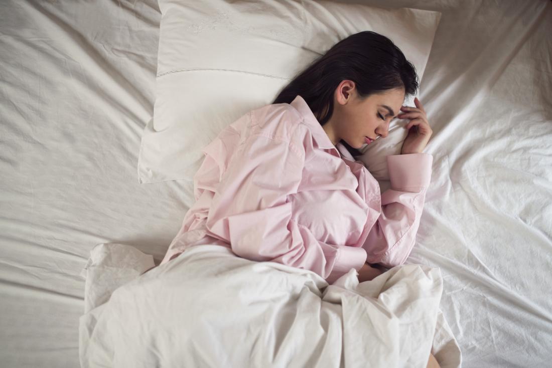 Жена в пижама, спяща от едната си страна в леглото.